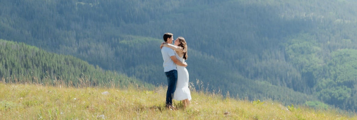 Belora Couple embracing on a grassy hill with mountains in the background